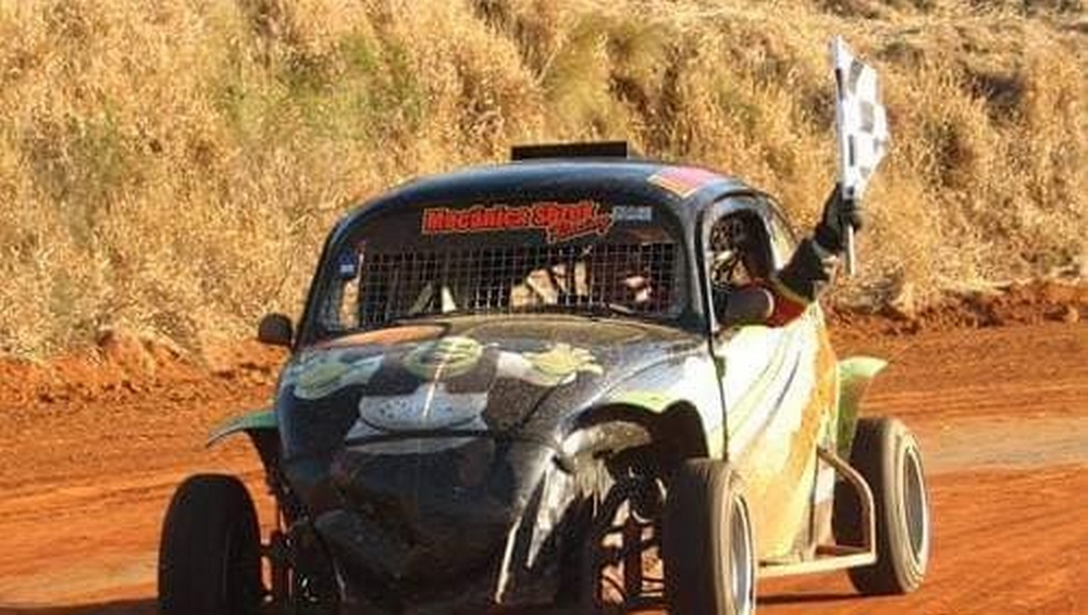 carro fusca com adesivo do personagem shrek no capô e com o motorista segurando uma bandeira quadriculada com o braço para fora do veículo