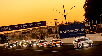 Vitor Genz NASCAR Londrina carros de corrida esportivos em fila com pôr do sol ao fundo e com telão escrito RandonCorp